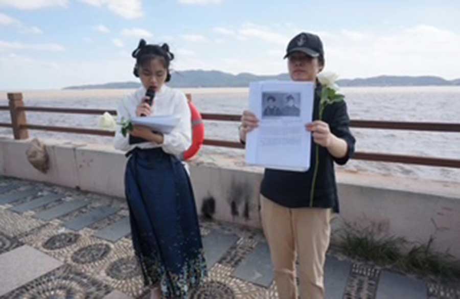 A young local girl narrates a tribute written by Anne Kelly to her Uncle Maurice Kelly whilst another girl exhibited his photograph, 2nd of October 2022, the 80th anniversary of the sinking of the Lisbon Maru, at the site of the memorial for Dongji fishermen's rescue of British Prisoners of War